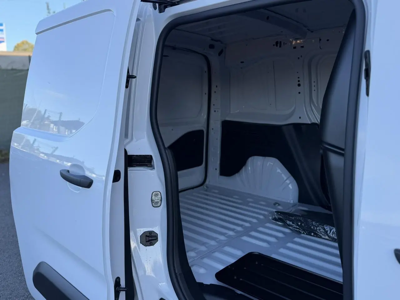 Vue latérale gauche sur l'ouverture de la porte coulissante d'un Peugeot Partner blanc Icy, montrant l'intérieur vide du coffre.