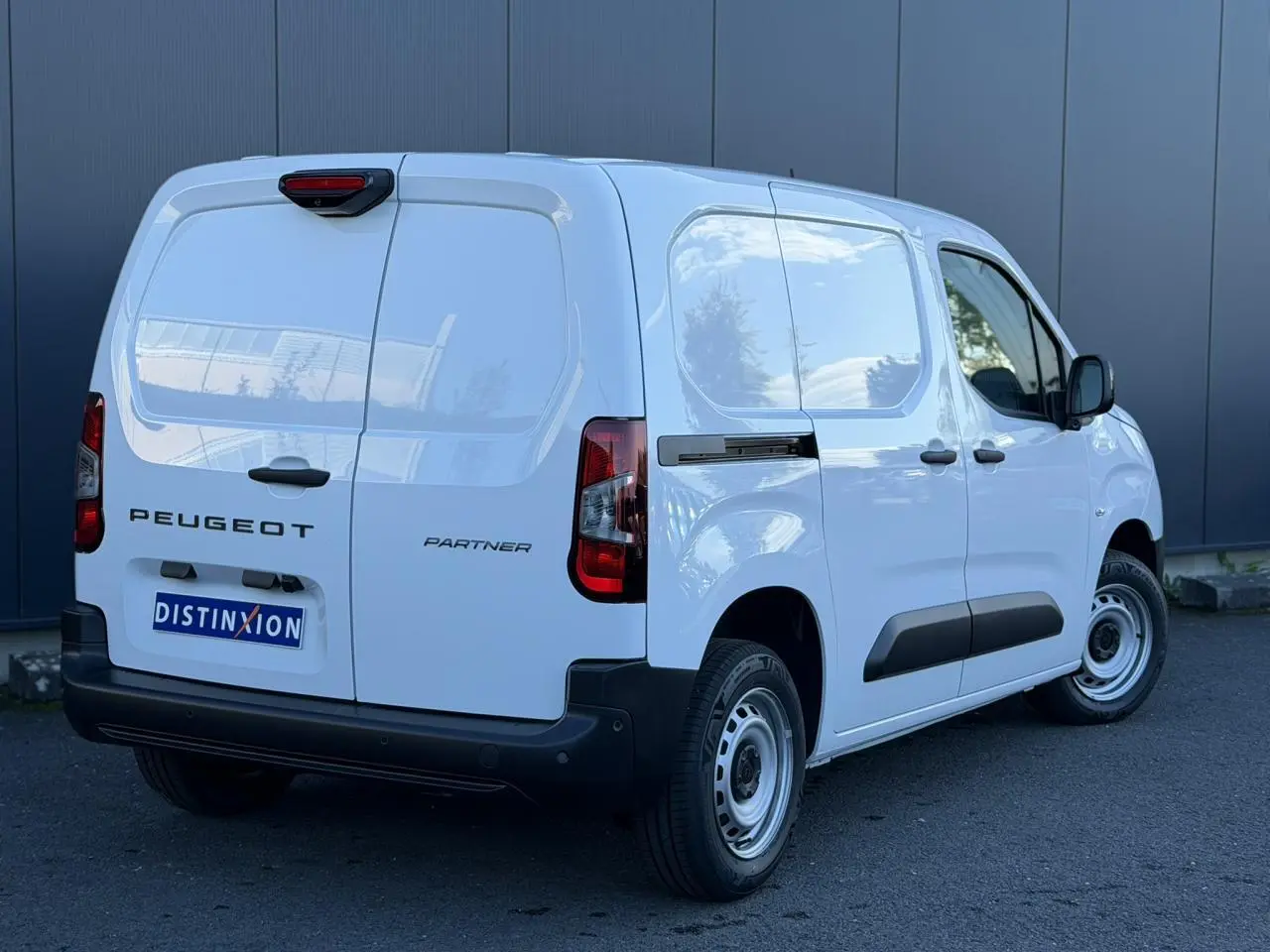 Vue 3/4 arrière droite du Peugeot Partner blanc Icy avec portes arrière battantes et protections latérales noires.