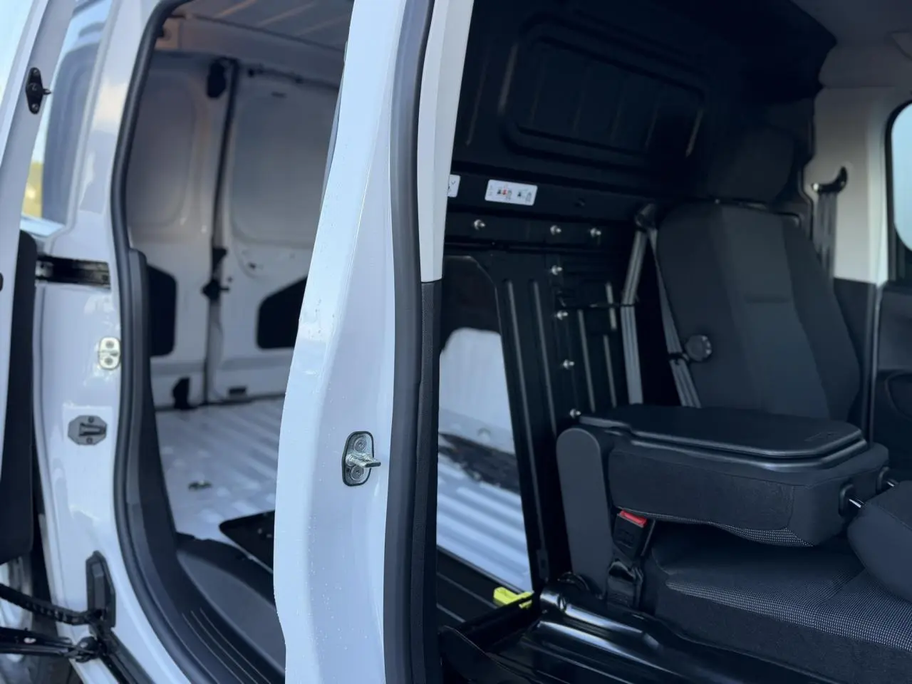 Vue intérieure côté droit du Peugeot Partner blanc Icy 2026 avec porte coulissante ouverte et banquette passager rabattue.