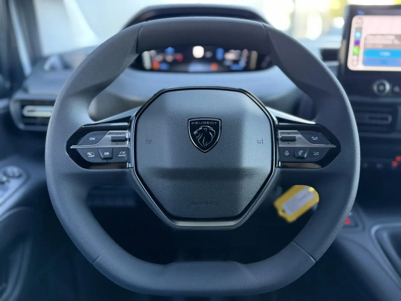 Vue rapprochée du volant noir multifonctions du Peugeot Partner 2026 avec combiné numérique flou en arrière-plan.