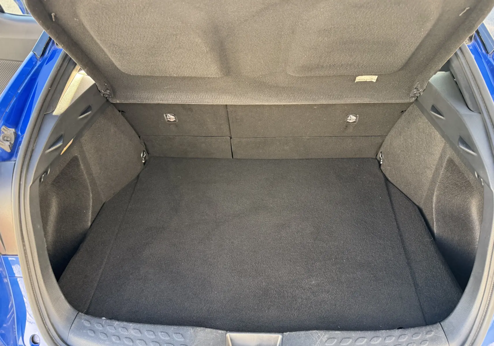 Coffre ouvert d'un Toyota C-HR 1.8 Hybrid bleu Nebula, montrant un espace de chargement propre et spacieux.