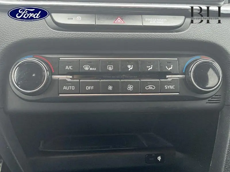 Panneau de commande de climatisation noir avec boutons et molettes, intérieur d'une Ford, vue frontale rapprochée.