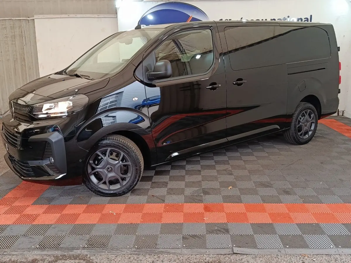 Vue 3/4 avant gauche d’un Citroën Jumpy XL noir avec phares allumés et jantes noires, stationné en intérieur.
