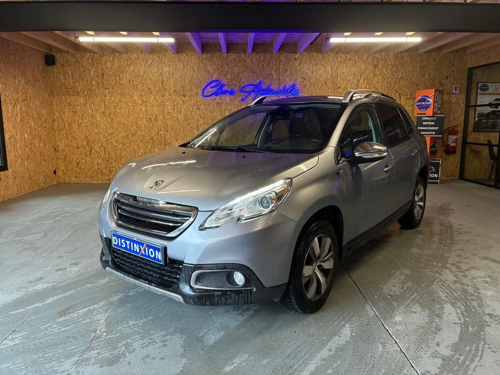 Peugeot 2008 gris vue 3/4 avant droit dans un garage, avec toit ouvrant et jantes alliage visibles.