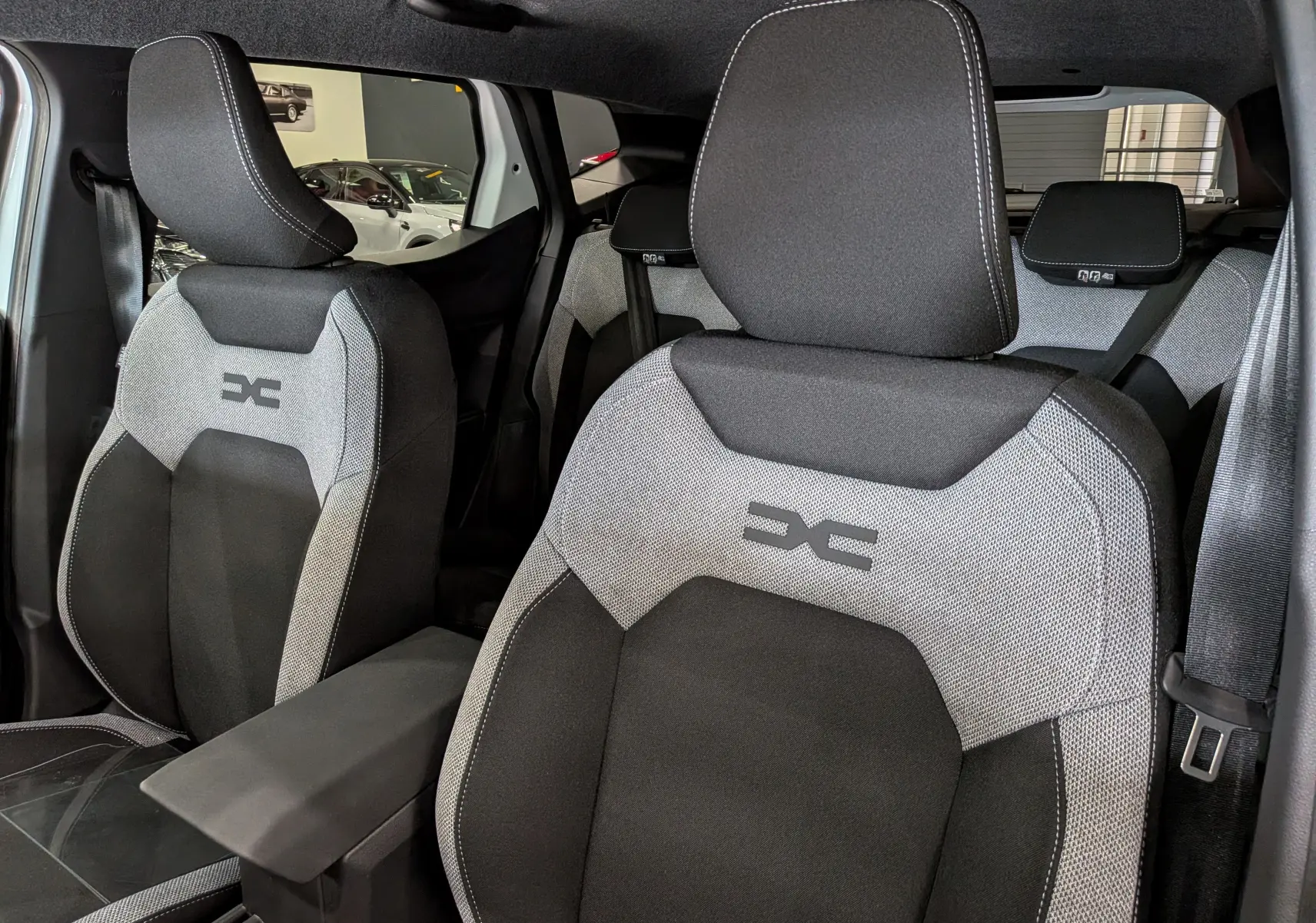 Vue intérieure rapprochée des sièges avant gris et noirs du Dacia Duster Hybrid-G 150 CH 4x4, avec logo distinctif brodé.