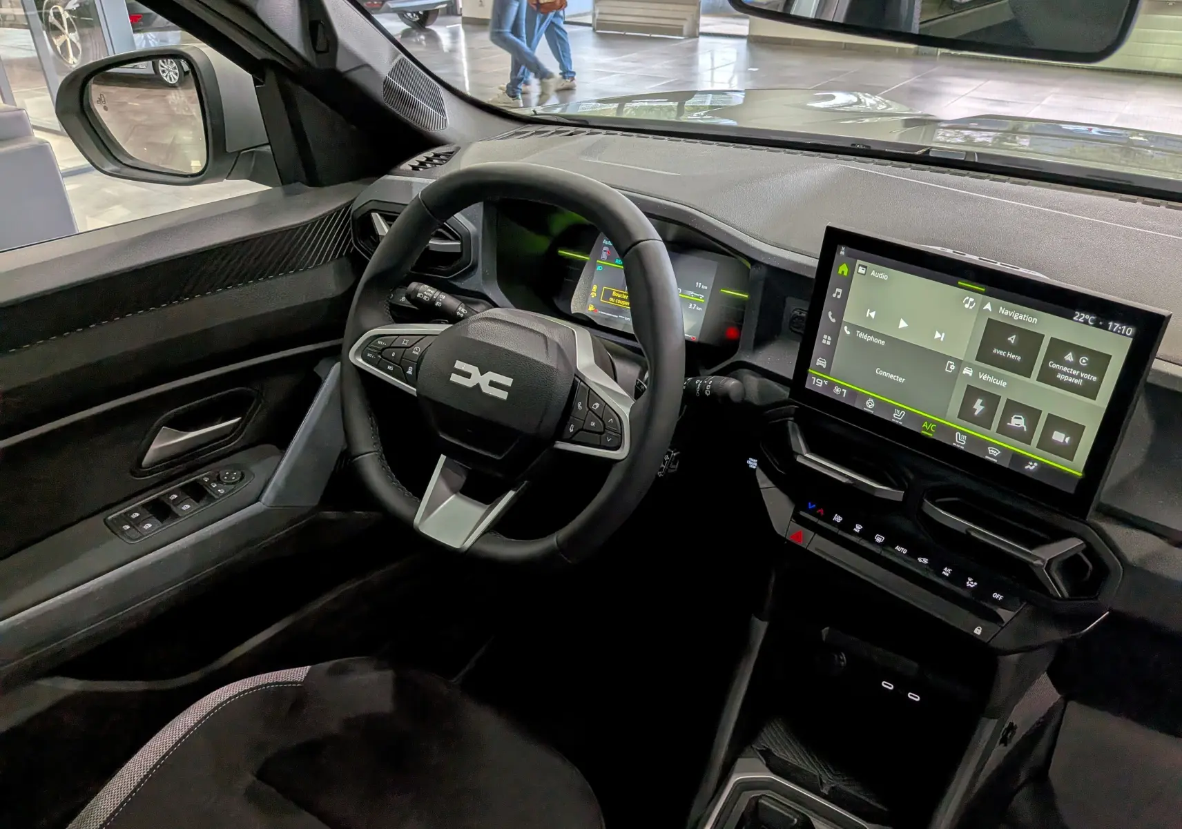 Vue intérieure côté conducteur du Dacia Duster Hybrid-G 150 CH 4x4 blanc Glacier, avec tableau de bord numérique et écran tactile central.