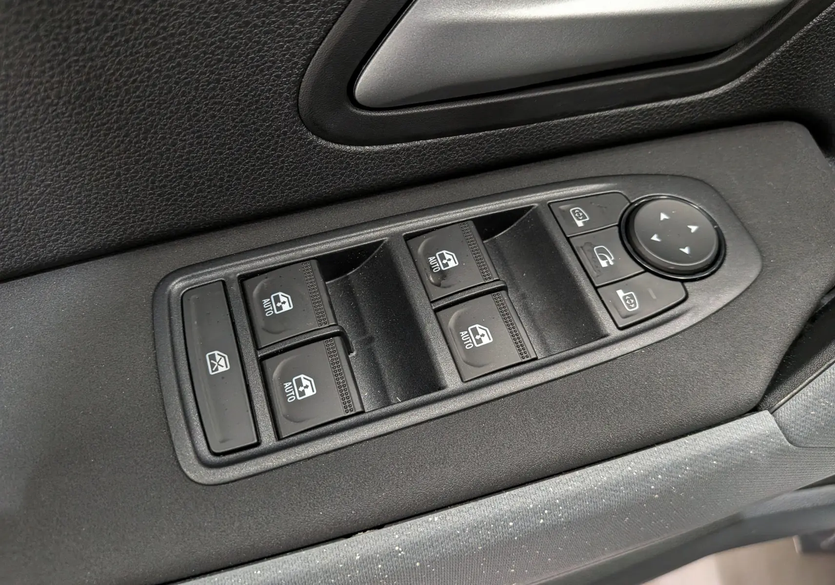 Gros plan sur les commandes des vitres électriques et rétroviseurs sur la porte côté gauche du Dacia Duster Hybrid-G blanc.