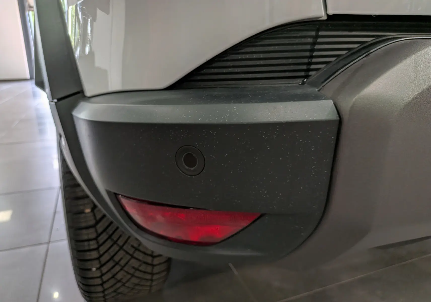 Gros plan sur le pare-chocs arrière droit blanc glacier du Dacia Duster Hybrid-G 150 CH 4x4 avec feu rouge et capteur de recul.