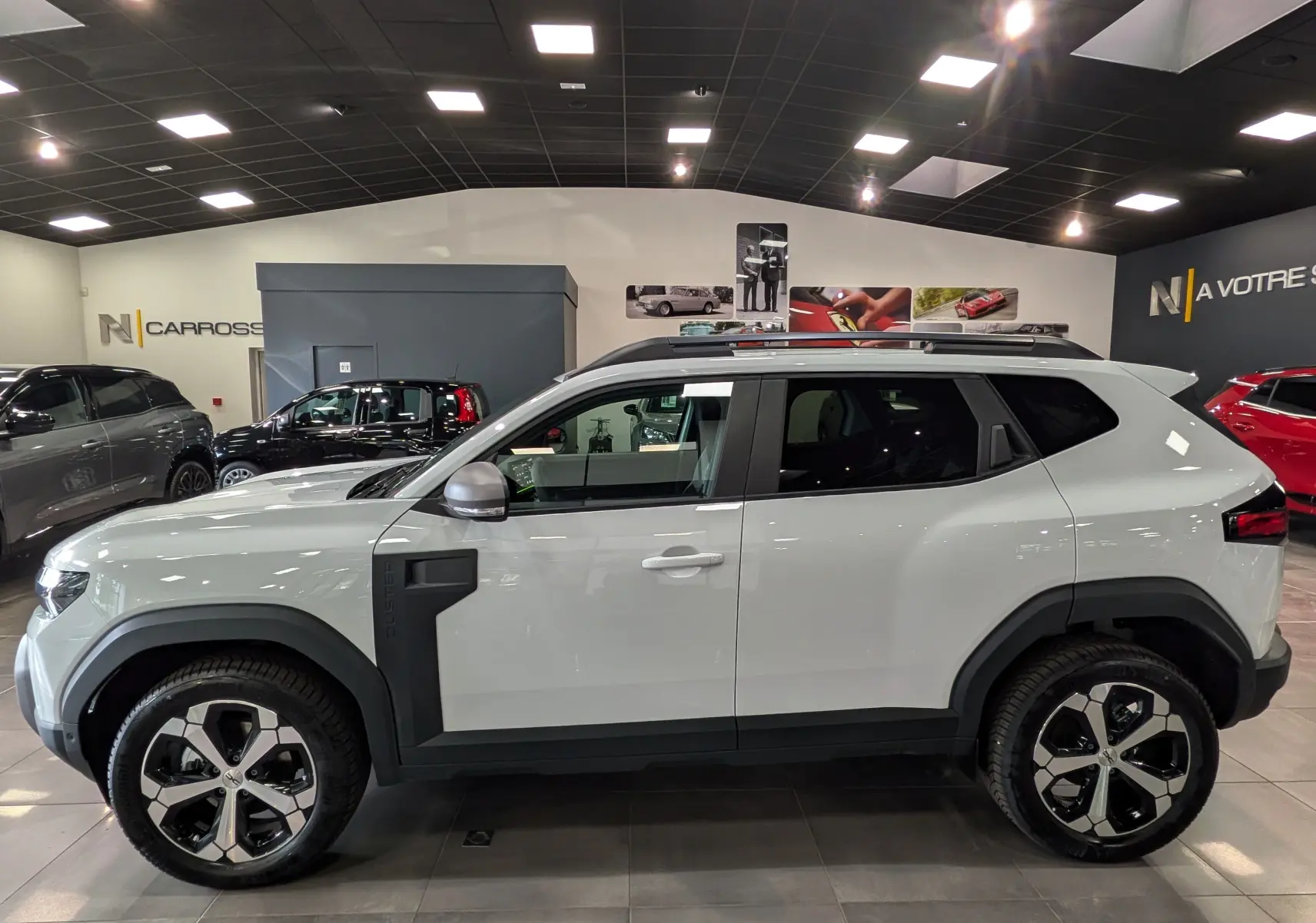 Vue profil droit du Dacia Duster Hybrid-G blanc glacier, avec jantes bi-ton noires et éléments noirs contrastants.