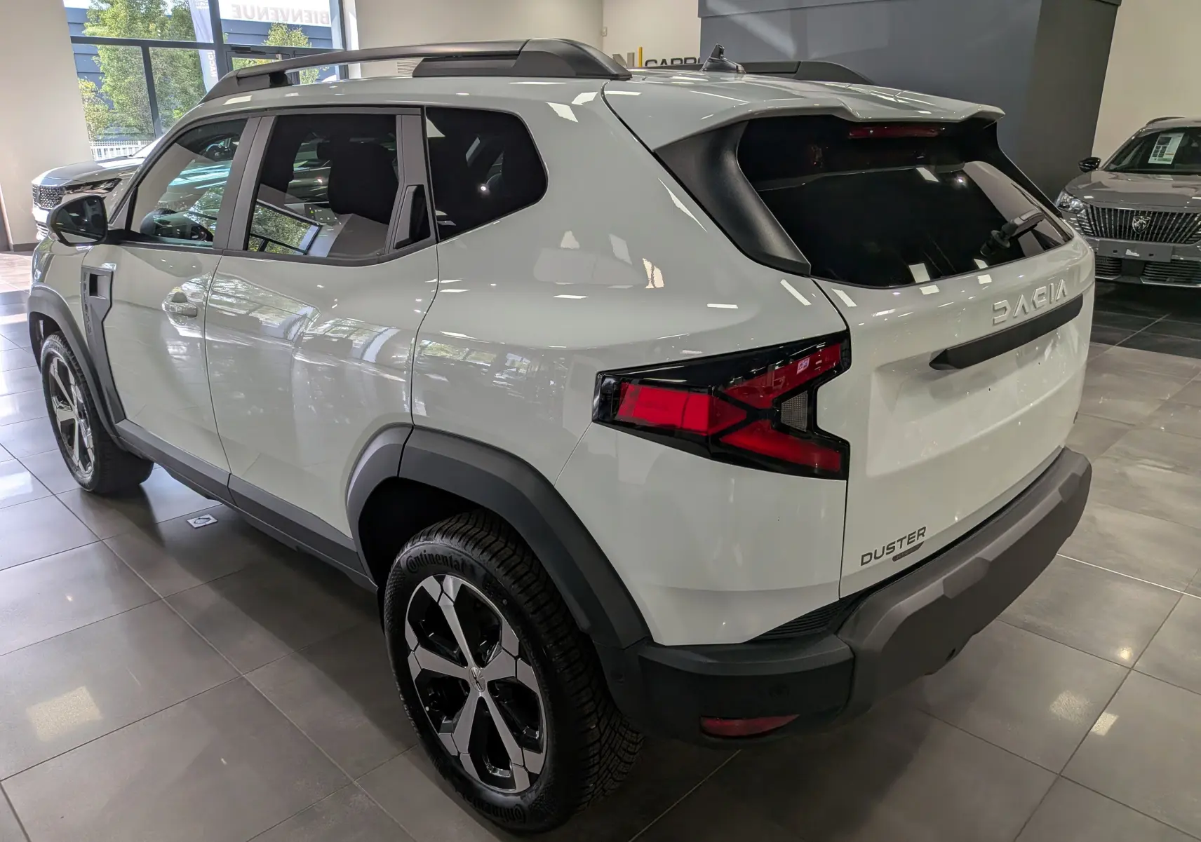 Vue 3/4 arrière droite du Dacia Duster blanc Glacier, soulignant ses feux arrière au design anguleux et ses jantes bi-ton.