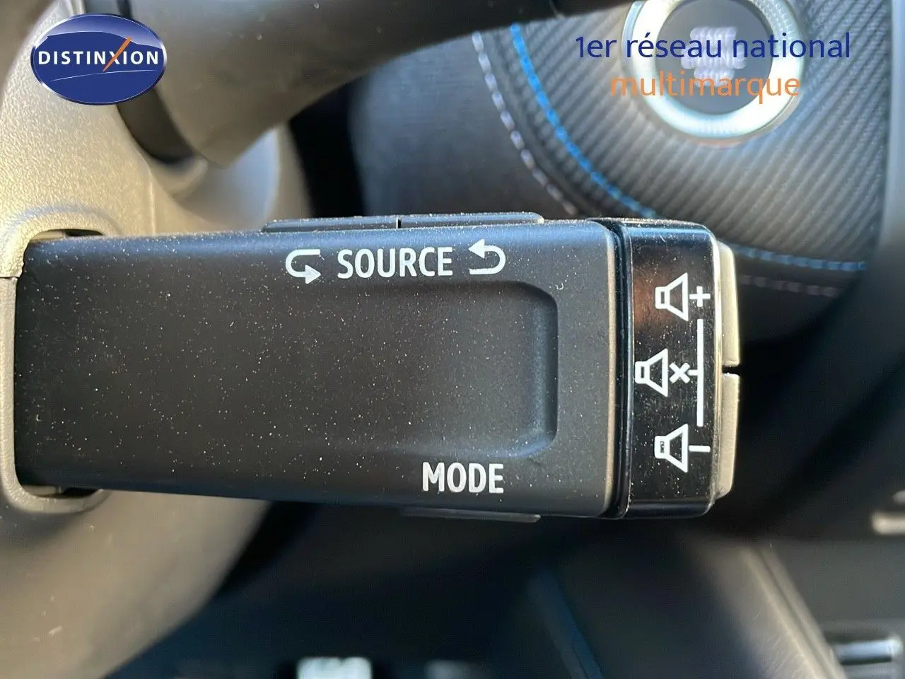 Gros plan sur la commande au volant du Renault Captur E-Tech hybride 2025, avec surpiqûres bleues visibles en arrière-plan.