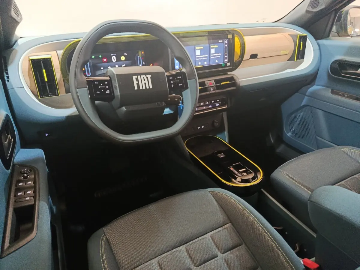 Vue intérieure avant droite de la Fiat Grande Panda 1.2 Hybrid 2025, tableau de bord beige et bleu avec écran tactile et volant carré.
