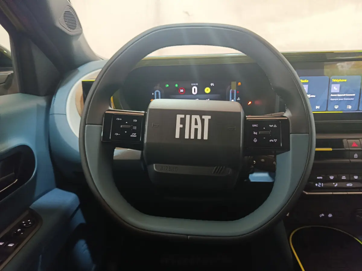 Vue intérieure centrée sur le volant bleu clair de la Fiat Grande Panda 2025 avec tableau de bord numérique et écran tactile.