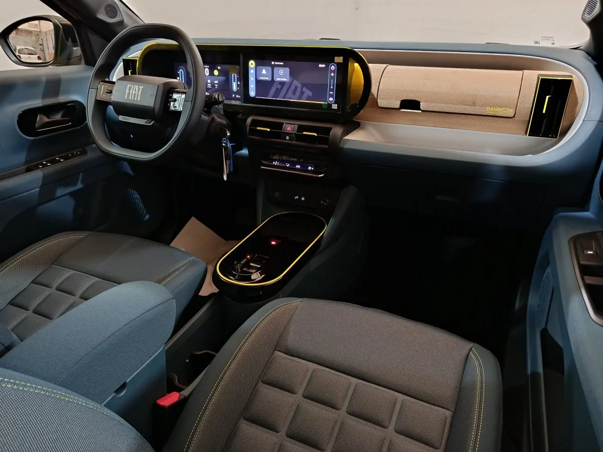 Vue intérieure avant droite de la Fiat Grande Panda jaune, tableau de bord moderne avec écran tactile et volant cuir noir.