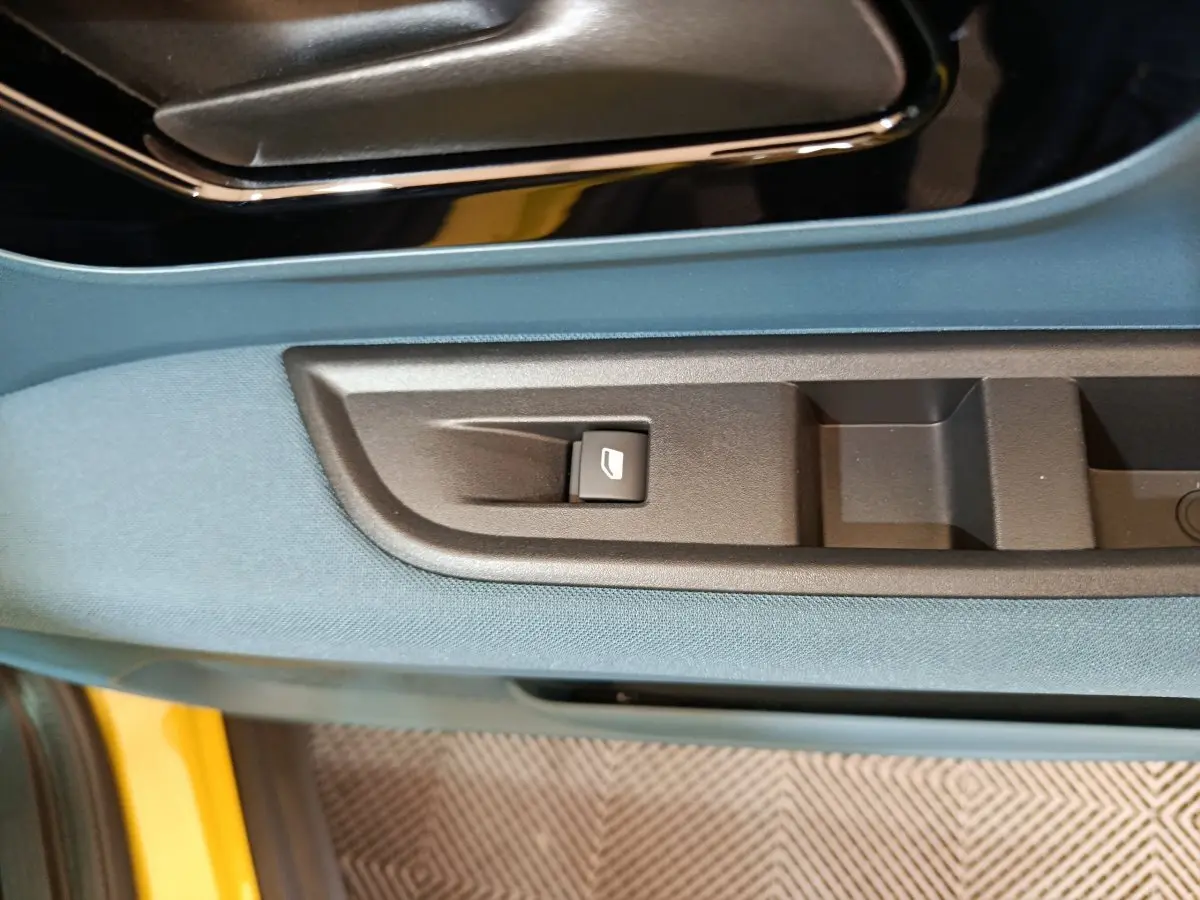 Détail de la commande de vitre sur la porte côté conducteur d’une FIAT Grande Panda jaune avec habillage bleu.