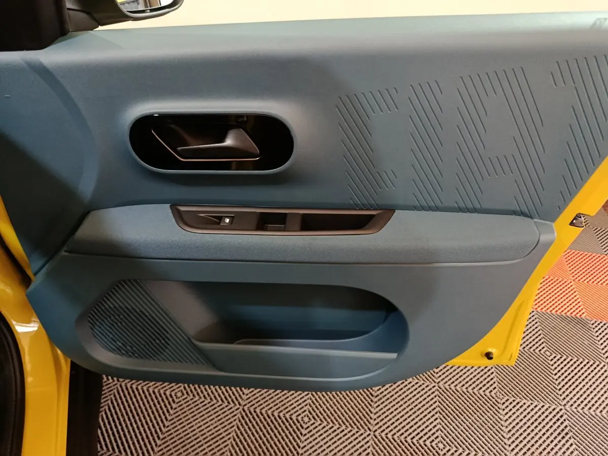 Vue intérieure côté gauche de la porte avant jaune de la FIAT Grande Panda avec garniture bleue et poignée noire.