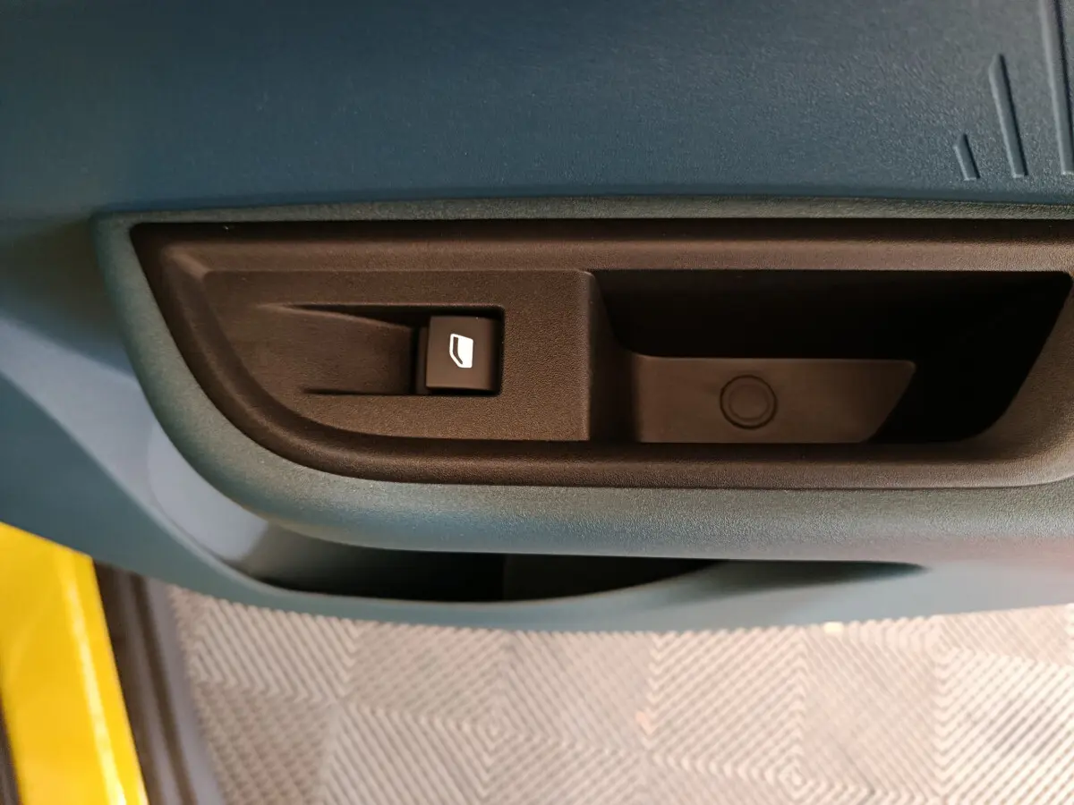 Gros plan sur la commande de lève-vitre côté conducteur d'une Fiat Grande Panda jaune, intérieur bleu-gris.