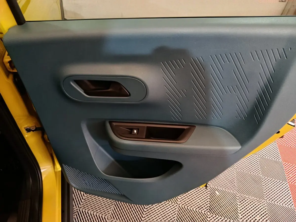 Vue rapprochée de la porte intérieure côté conducteur de la Fiat Grande Panda jaune avec logo FIAT en relief.