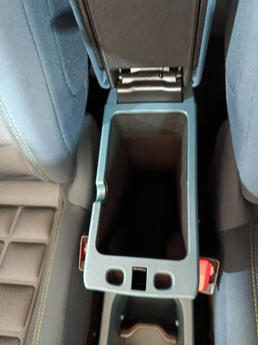 Vue plongeante sur la console centrale ouverte entre les sièges avant bleu foncé de la Fiat Grande Panda jaune.