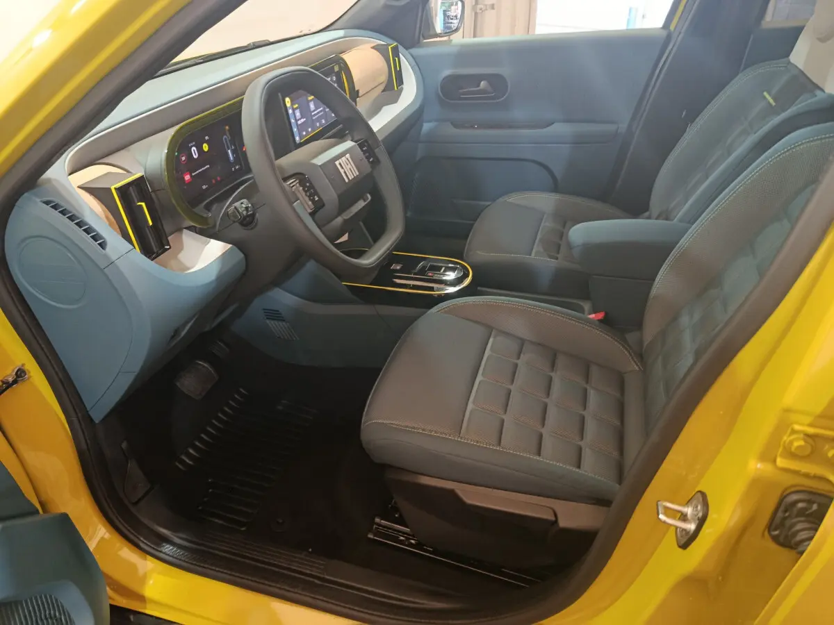 Intérieur avant droit de la FIAT Grande Panda jaune 2025, volant cuir, tableau de bord digital et sièges gris matelassés.
