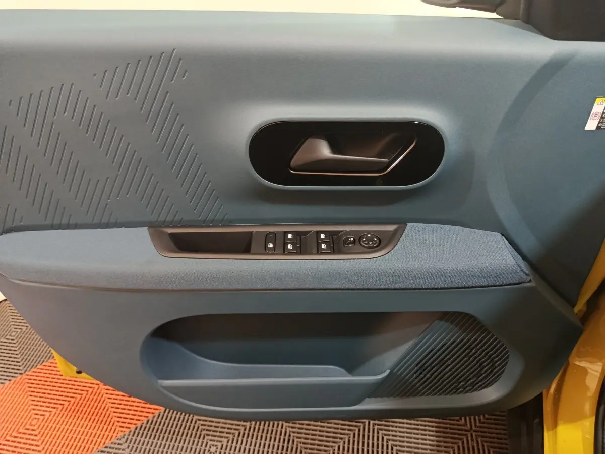 Vue intérieure côté gauche de la porte avant d’une FIAT Grande Panda jaune avec garniture bleue et commandes électriques.