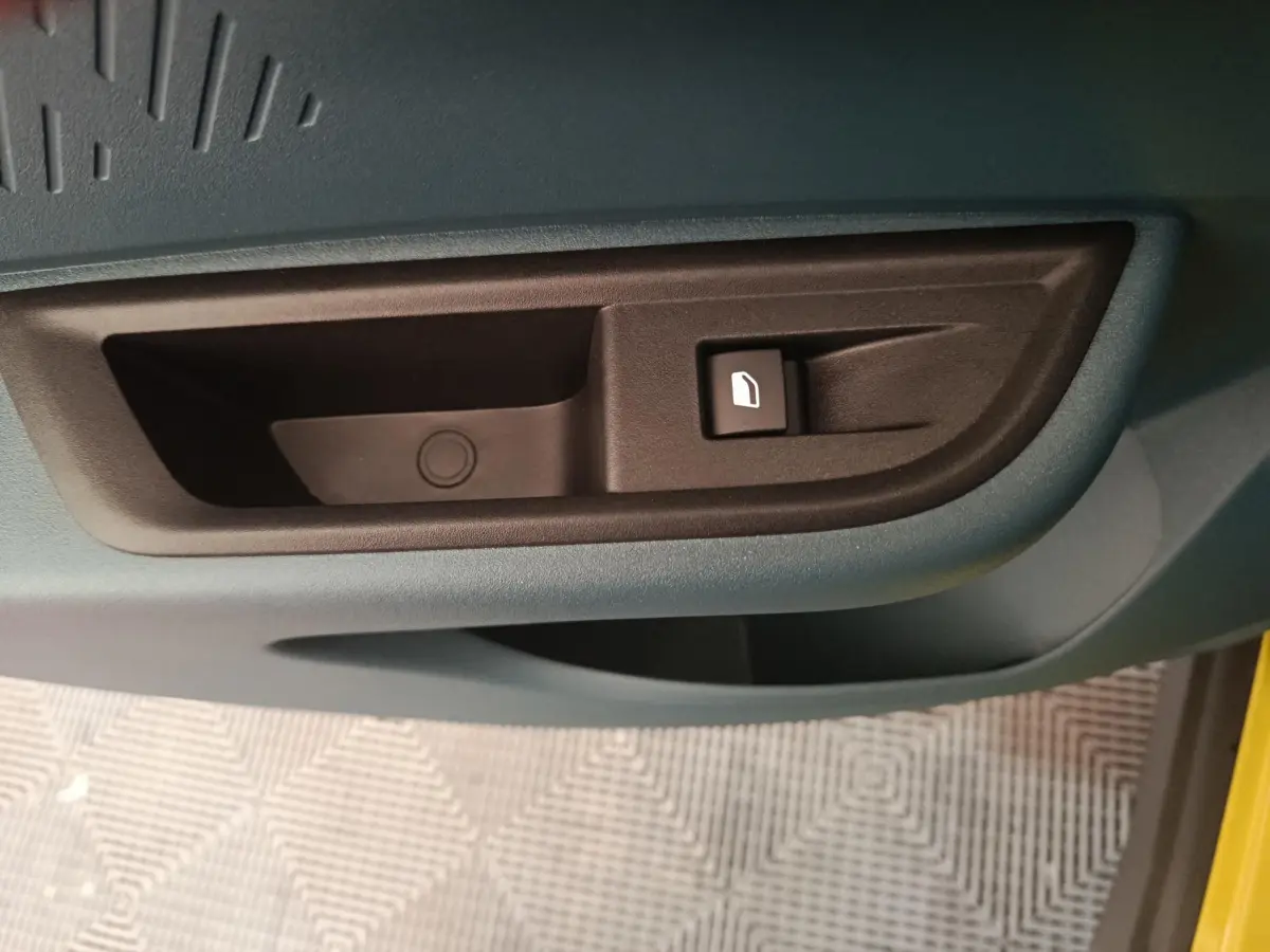 Détail de la poignée intérieure de porte noire sur fond bleu de la FIAT Grande Panda jaune 2025, côté conducteur.