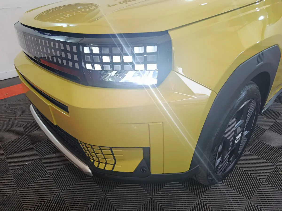 Gros plan sur l'avant droit jaune vif de la FIAT Grande Panda 2025 avec phares LED allumés et jante noire distinctive.