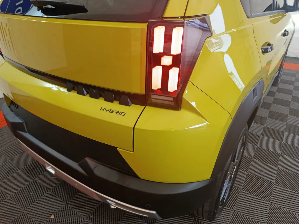 Vue 3/4 arrière droite d'une FIAT Grande Panda jaune 2025 avec feux arrière LED et badge Hybrid visible.