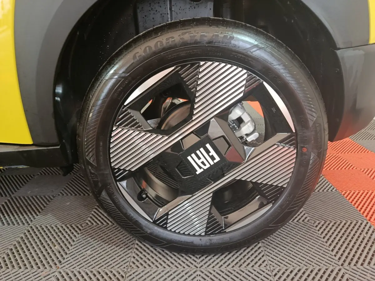Gros plan sur la roue avant droite d’une FIAT Grande Panda jaune, jante noire et argent au design géométrique.