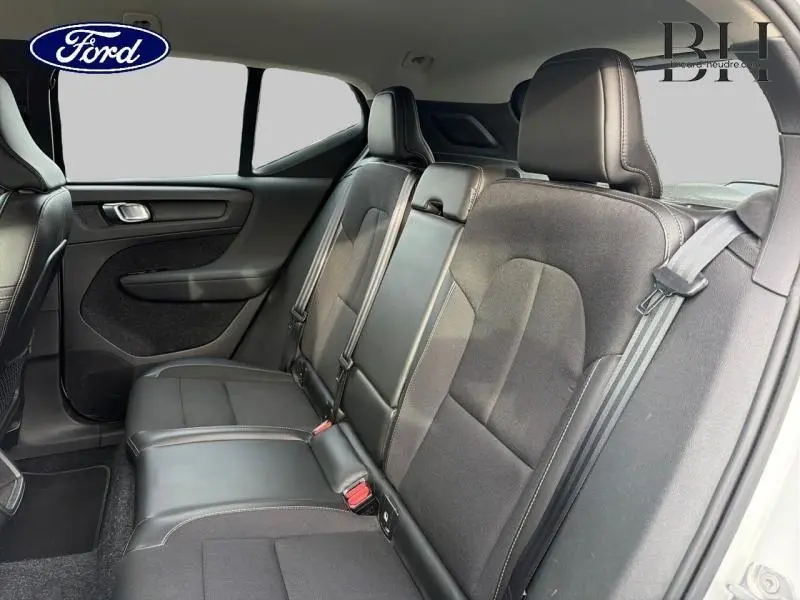 Vue intérieure de la banquette arrière en tissu noir du Volvo XC40 blanc, avec ceintures de sécurité et appuie-têtes visibles.