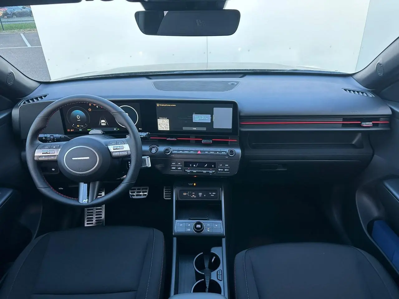 Intérieur avant du Hyundai Kona 2025 noir Abyss, tableau de bord numérique et écran tactile large avec touches rouges décoratives.