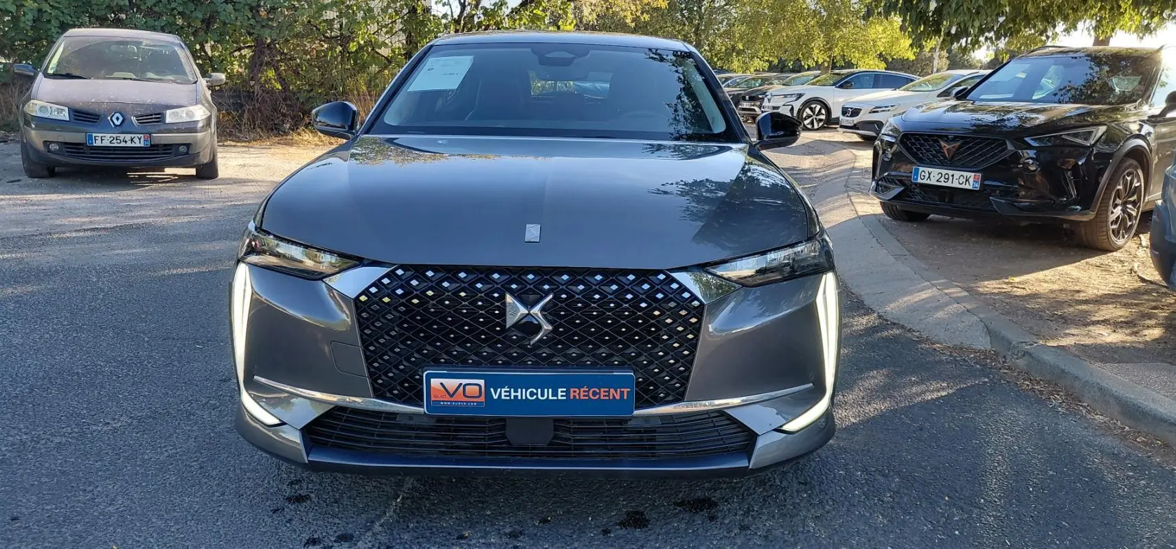 Vue frontale d'une DS4 hybride gris métallisé avec calandre noire à motifs losanges et feux diurnes verticaux allumés.