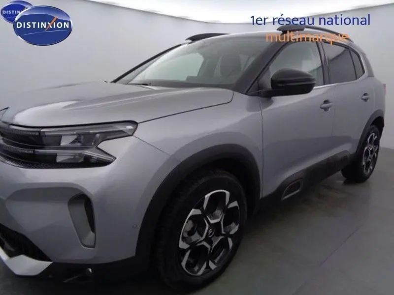 Vue 3/4 avant droit d'un Citroën C5 Aircross gris acier avec jantes alu et barres de toit noires.