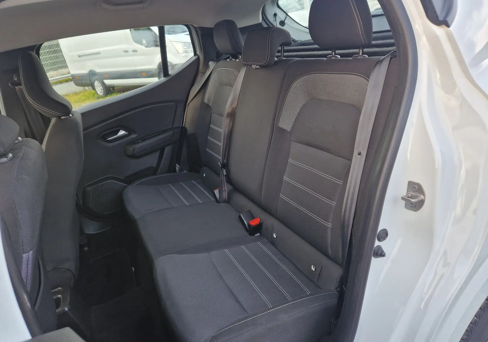 Vue intérieure arrière côté droit de la Dacia Sandero blanche 2022, montrant les sièges arrière en tissu noir avec surpiqûres grises.