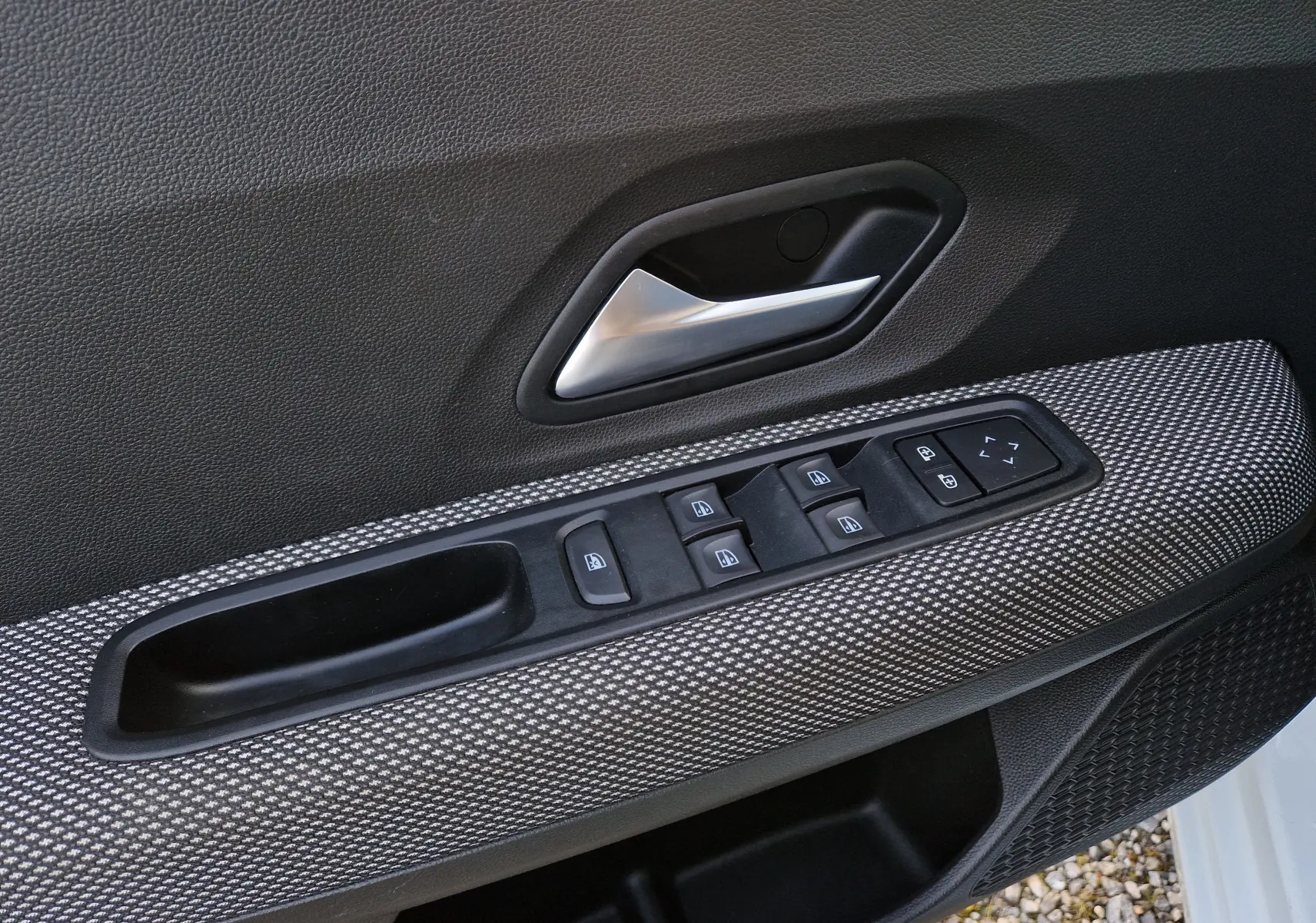 Gros plan sur la commande des vitres et la poignée intérieure côté conducteur d’une Dacia Sandero blanche 2022.