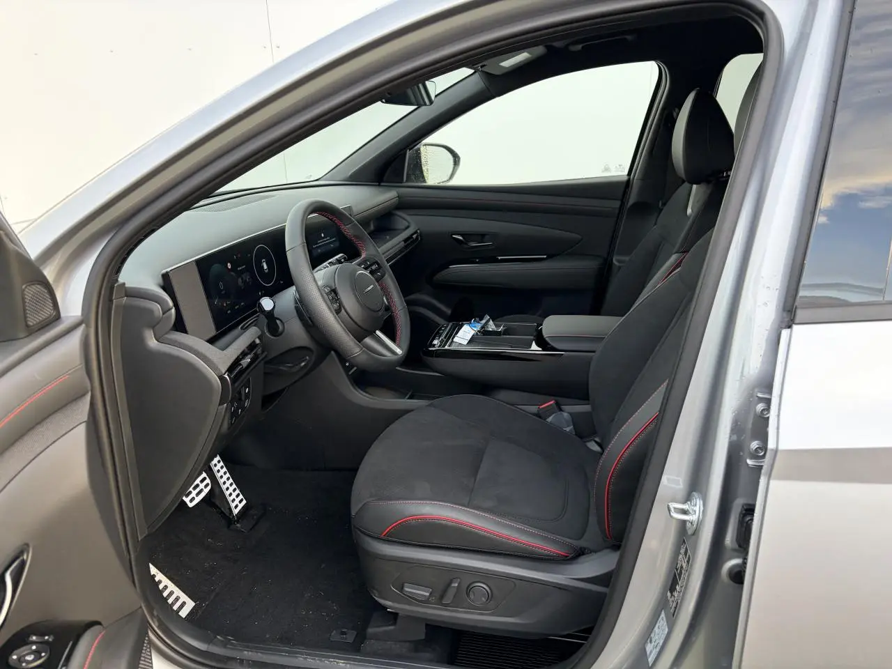 Vue intérieure côté conducteur du Hyundai Tucson 2025 argent, sièges cuir/alcantara noirs avec surpiqûres rouges et volant sport N Line.
