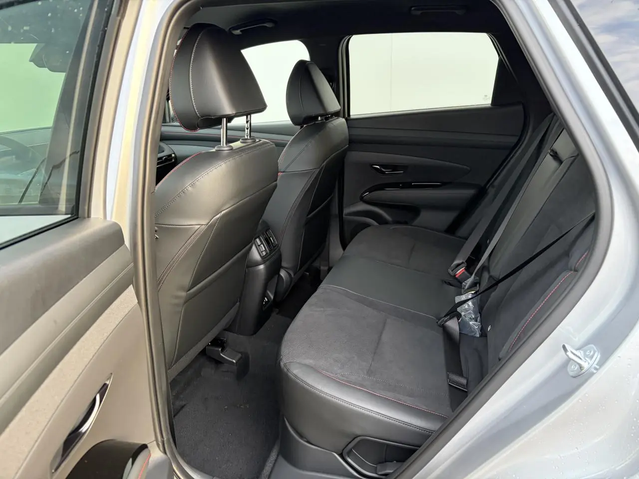 Vue côté droit de l'habitacle arrière du Hyundai Tucson 2025 en Shimmering Silver, sellerie cuir/alcantara noire avec surpiqûres rouges.