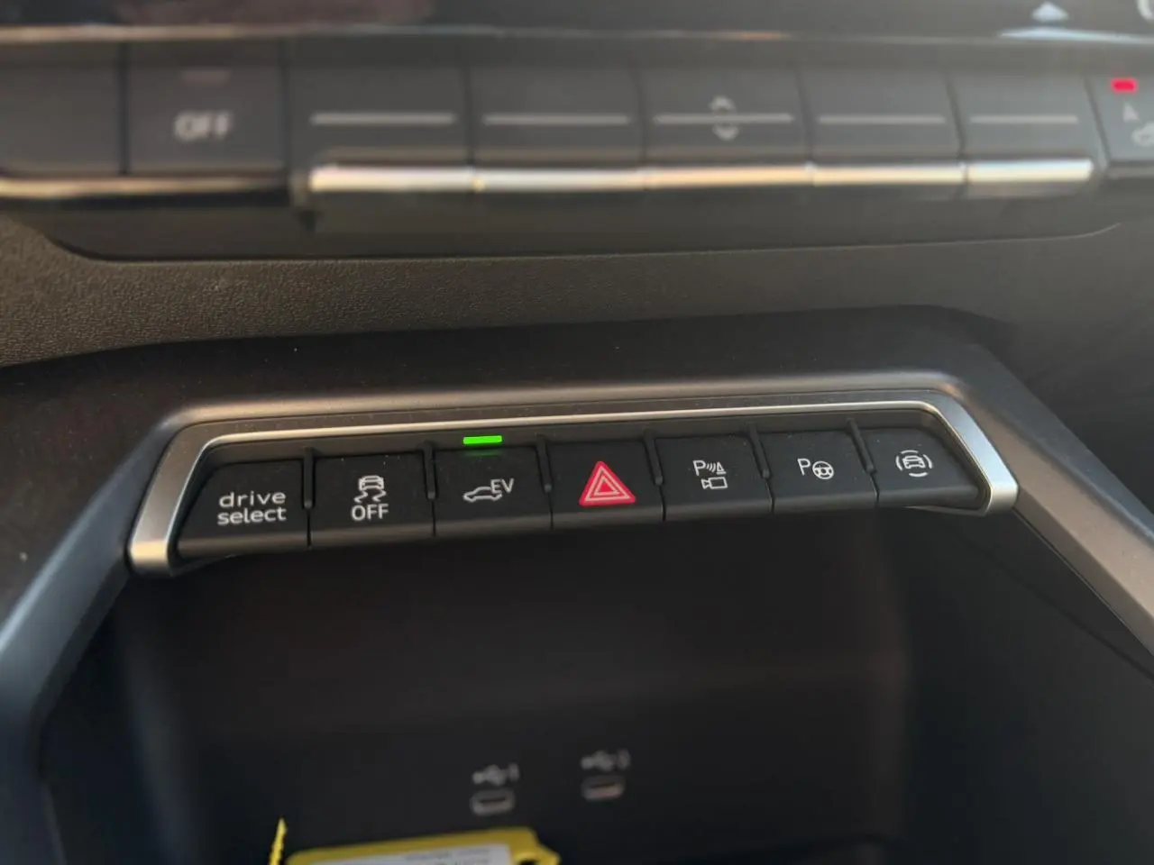 Gros plan sur la rangée de boutons de commande au centre de la console d'une Audi A3 Sportback noire, avec indicateur vert allumé.