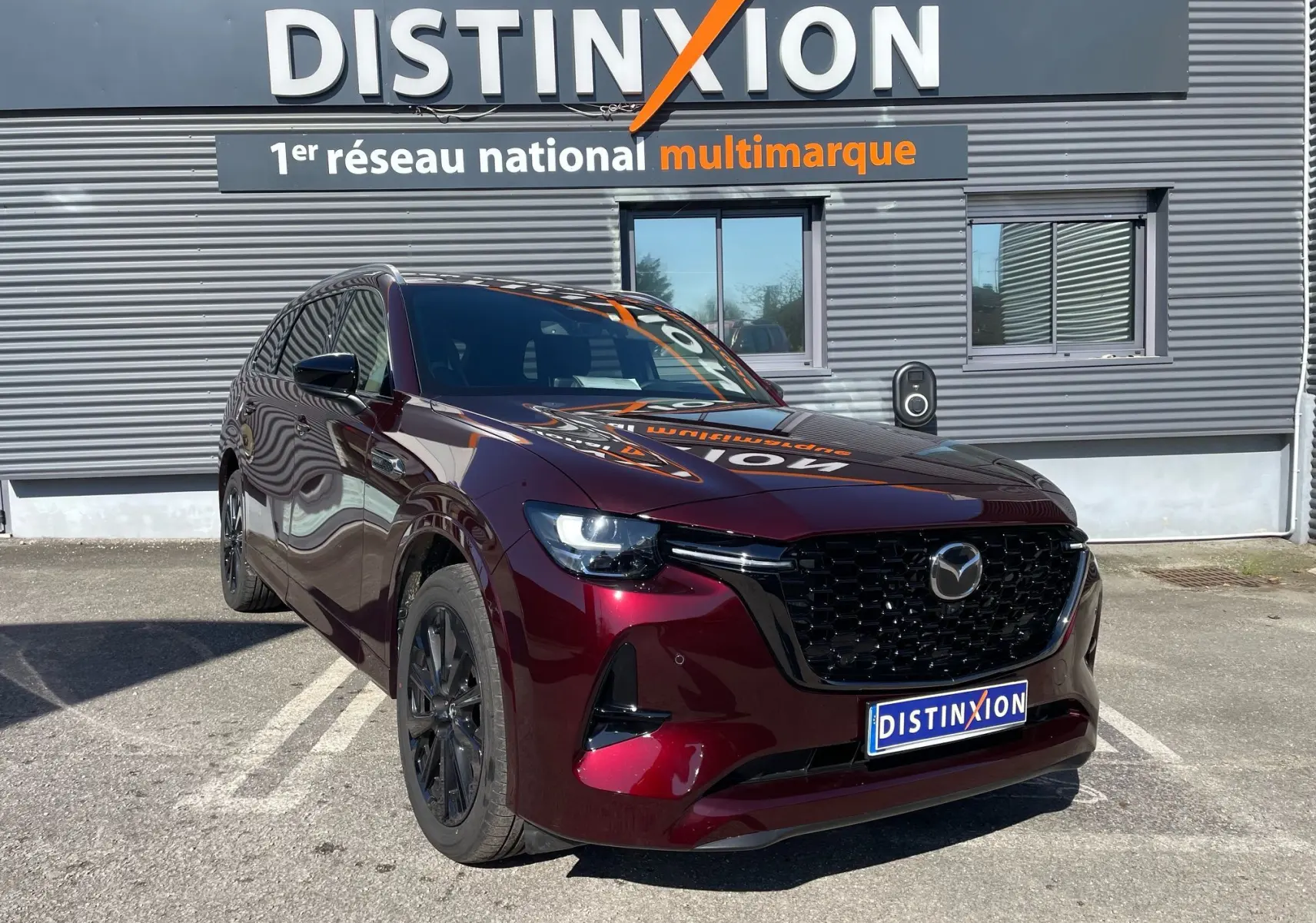 Vue 3/4 avant du Mazda CX-80 hybride rechargeable en rouge Artisan, avec calandre noire et jantes foncées.