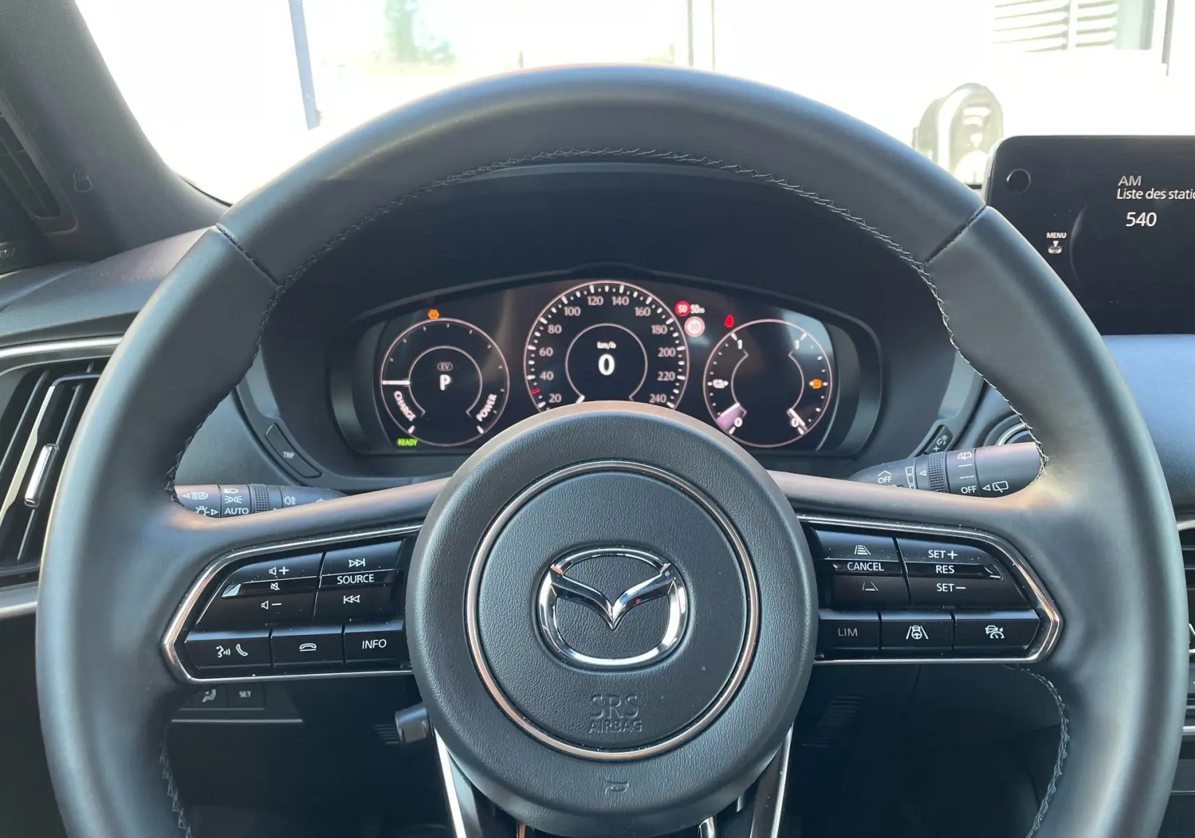 Vue rapprochée du volant cuir noir du Mazda CX-80 2024 avec commandes intégrées et tableau de bord numérique.