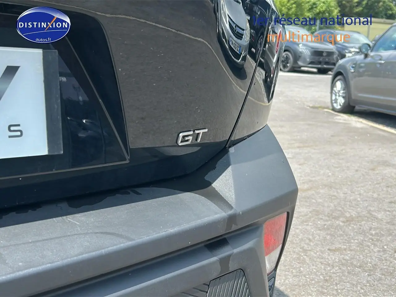 Gros plan sur le logo GT à l'arrière droit d'une Peugeot 408 Hybrid 145 GT noire 2024 en extérieur.