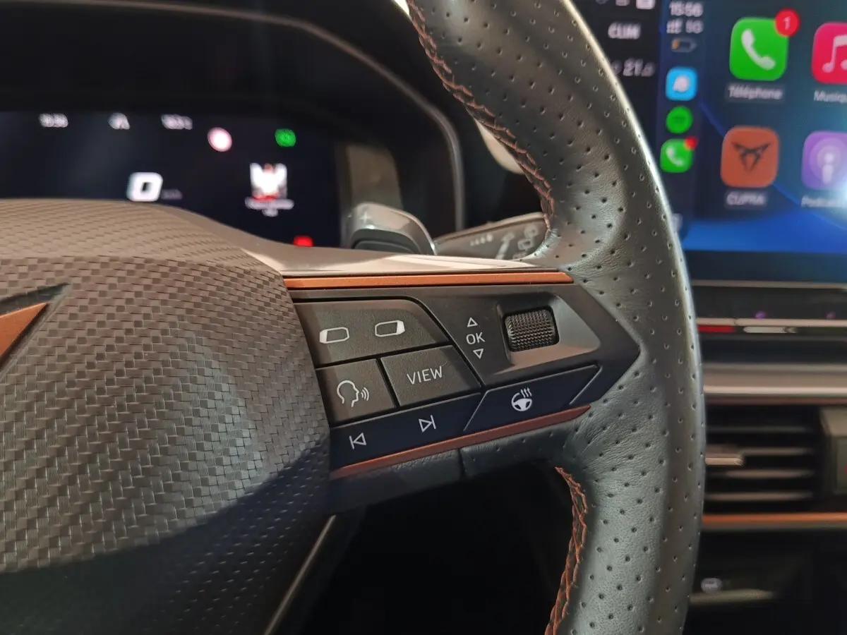 Gros plan sur le volant noir perforé du CUPRA Formentor 2024 avec commandes multifonctions et écran tactile en arrière-plan.