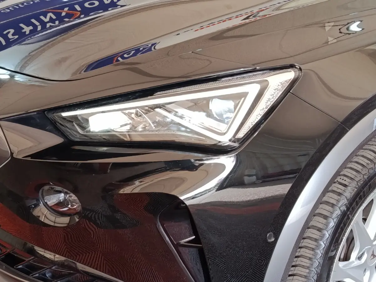 Gros plan sur le phare avant gauche noir brillant du CUPRA Formentor 2024 avec jante et capteur de stationnement visible.