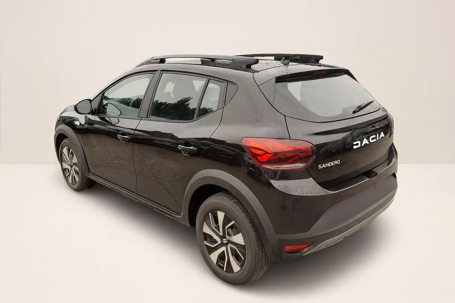 Vue 3/4 arrière droite d'une Dacia Sandero Stepway noire nacrée avec barres de toit et jantes 16 pouces.