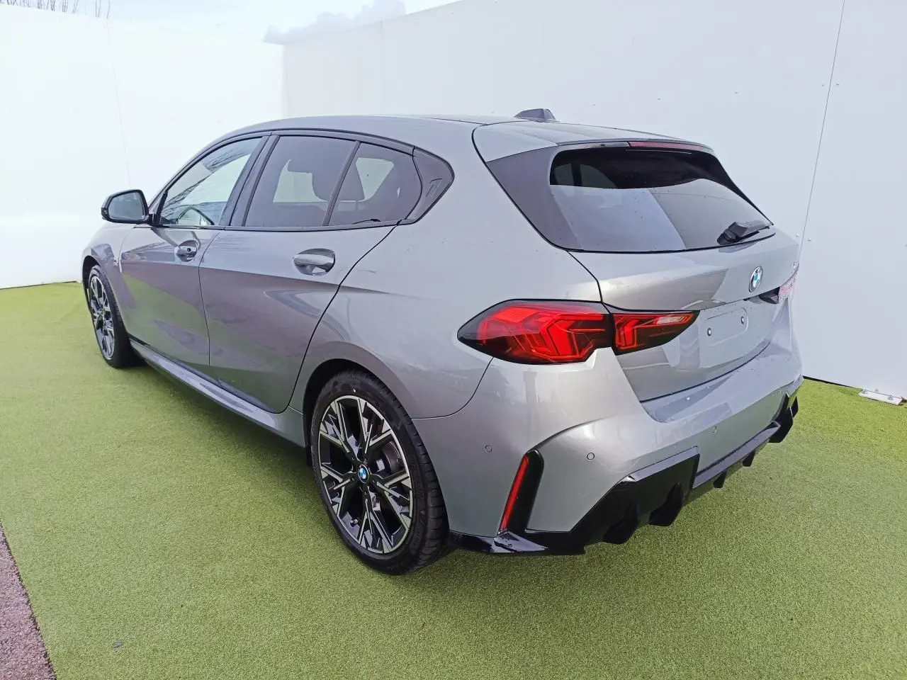 BMW Série 1 gris Skyscraper vue 3/4 arrière droit, toit noir, jantes 18 pouces bicolores et diffuseur arrière noir.