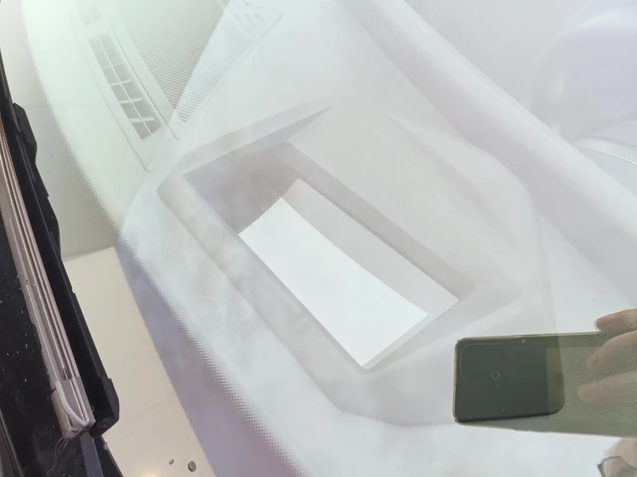 Vue intérieure du tableau de bord de la BMW Série 1 2025 gris Skyscraper avec écran et toit noir visible en reflet.