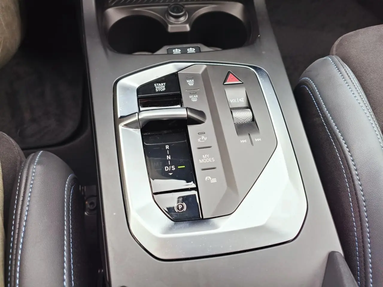 Vue rapprochée de la console centrale grise avec levier de boîte automatique et accoudoirs en Alcantara noir surpiqués bleus.