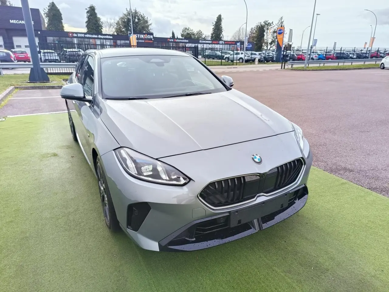BMW Série 1 F70 gris Skyscraper vue 3/4 avant gauche avec calandre noire et toit noir sur parking.