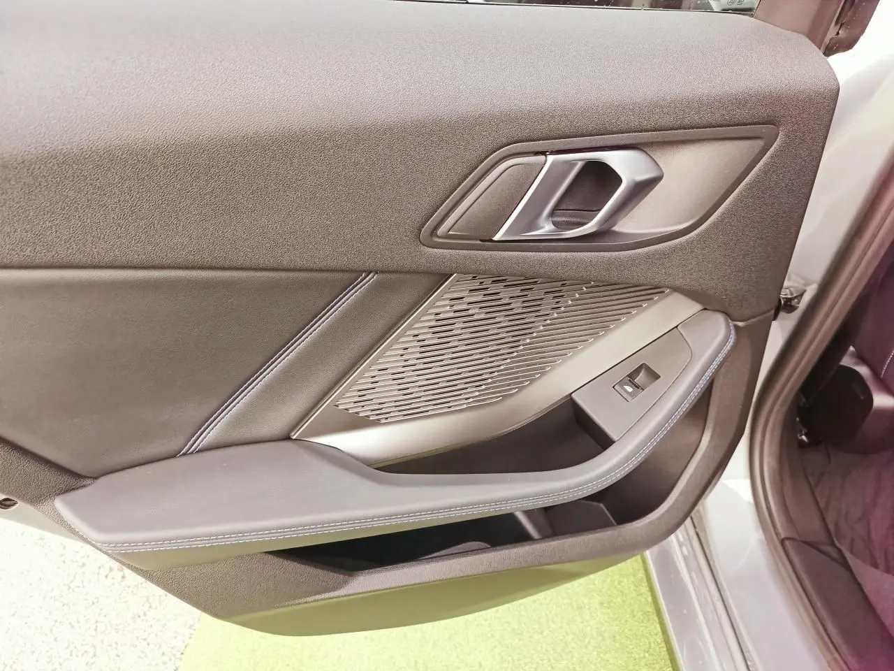 Vue rapprochée de la porte avant droite de la BMW Série 1 2025, habillage noir avec surpiqûres bleues et insert aluminium.