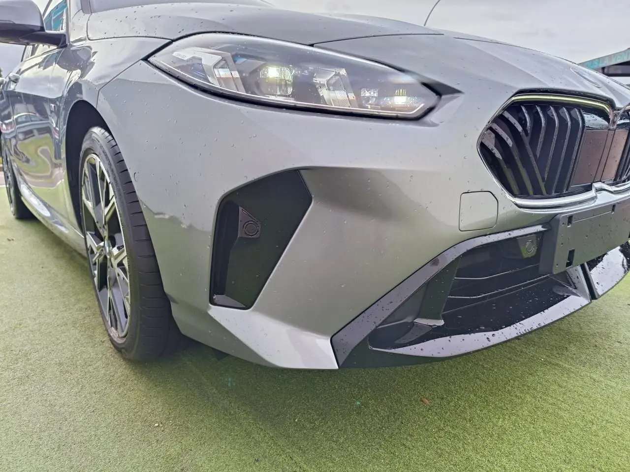 Gros plan sur l'avant droit d'une BMW Série 1 gris Skyscraper avec calandre noire et phares LED allumés.